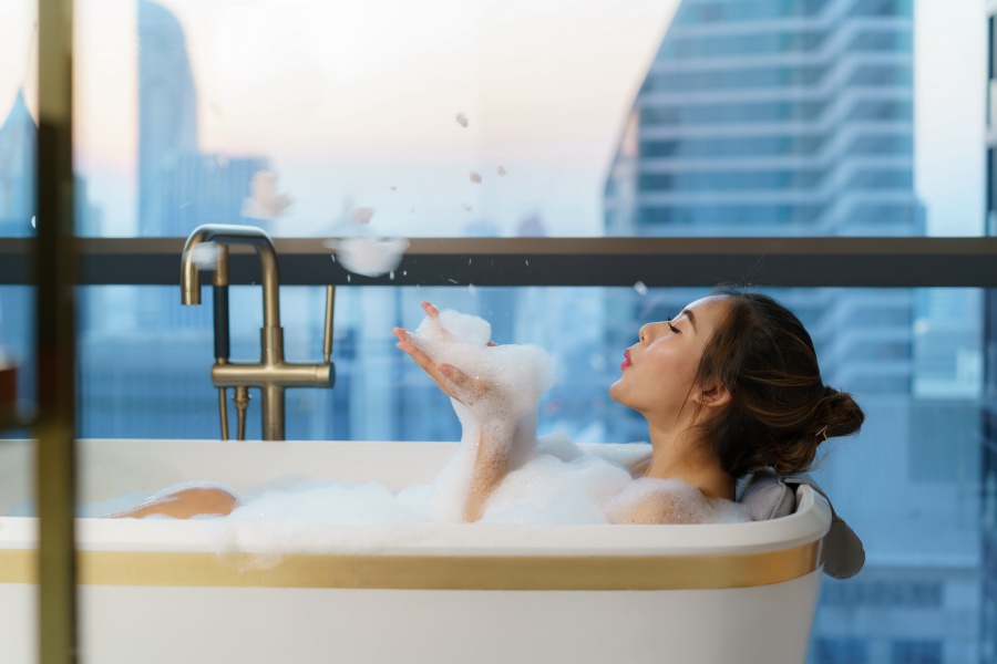 Asian woman takes a bath with soap bubble in bathtub at bathroom of luxury hotel in downtown city while on vacation.